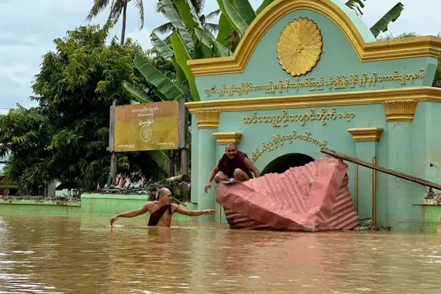 Seorang biksu Buddha melewati banjir sementara seorang biksu lainnya duduk di atap yang rusak di depan sebuah biara di Desa Sin Thay, di wilayah Naypyidaw, Myanmar, pada 13 September 2024. Banjir ini dipicu oleh Topan Yagi.