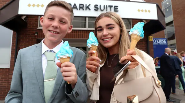 Dečak u odelu i devojčica u jakni drže sladolede u rukama i smeše se u kameru