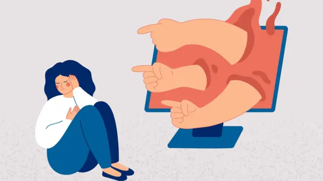 صورة تعبيرية لامرأة حزينة تجلس على الأرض أمام شاشة كمبيوتر تخرج منها أياد تشير أصابعها إليها