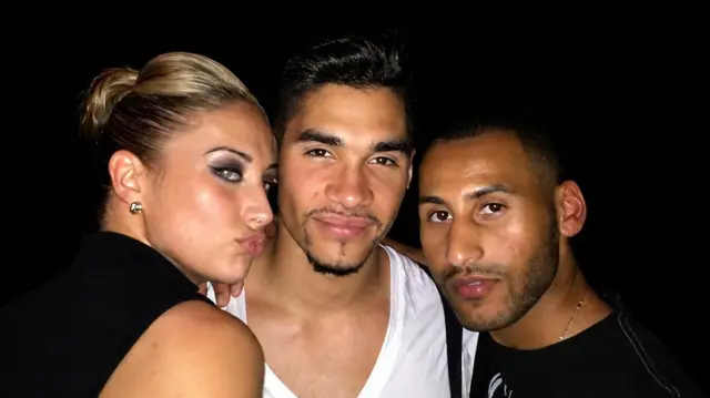 Bradshaw, oo xiran shaati madow, ayaa sawir kula jira Louis Smith oo xiran funaanad cad, iyo haweeney xiran dhar madow.