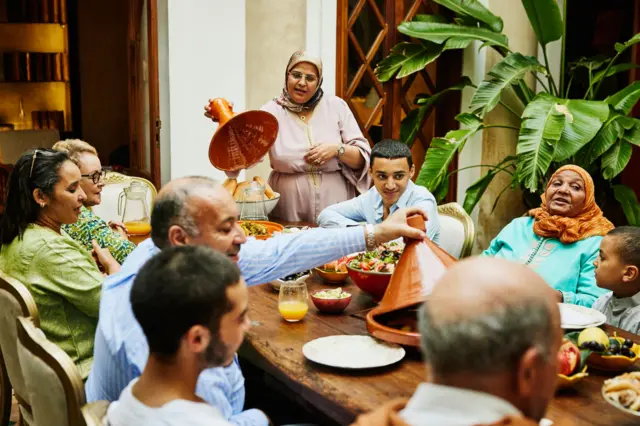 Plan large d'une famille multigénérationnelle marocaine servant le repas à table pour l'Eid.