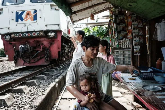 Seorang warga Jakarta menggendong anaknya di sebuah warung pinggir rel kereta api.