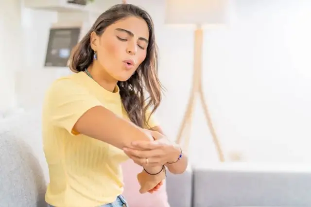 دختری آرنج دست راستش را گرفته به نشانه اینکه درد دارد