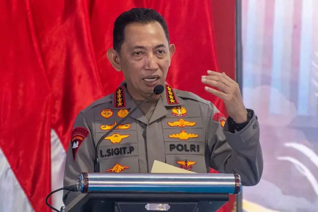 Kapolri Jenderal Pol Listyo Sigit Prabowo sedang berada di atas podium, mulutnya sedikit terbuka dan tangan kirinya naik ke atas sedang menjelaskan sesuatu.