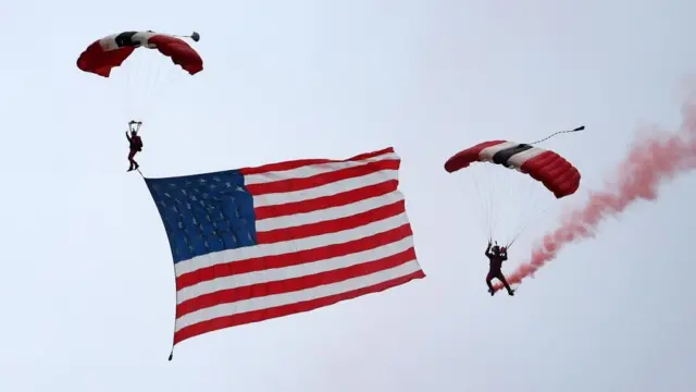 イギリス国旗の赤白青を模したパラシュート兵2人が空中を落下している。1人は足に大きなアメリカ国旗を括り付けて広げている。もう1人は足に発煙筒を着け、赤い煙をたなびかせている