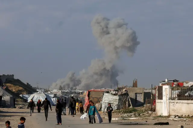 فلسطينيون يسيرون بينما يتصاعد الدخان بعد غارة إسرائيلية في خان يونس جنوب قطاع غزة، 13 أبريل/نيسان 2025.