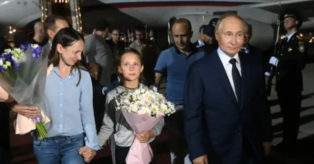 Foto mostra Vladimir Putin, uma criança e uma mulher, as duas descendo de um avião no período noturno, em cerimônia para receber herois do país que atuavam como supostos espiões no exterior