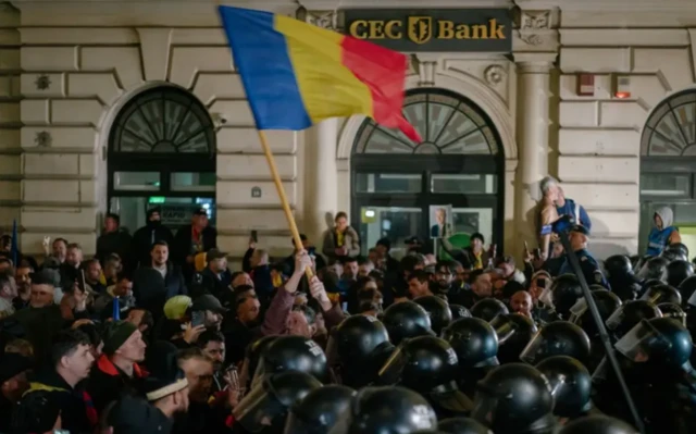 Georgescu'nun seçimlerde aday olamayacağının açıklandığı Mart ayındaki protestolardan birinde polisle göstericiler çok yakın duruyor. Fotoğrafta bir adet Romen bayrağı var. Polisler kask takmışlar.