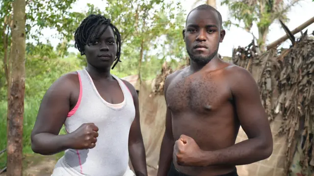 Lamono Evelyn porte un singlet blanc et Jordan Loverine pose torse nu, tous deux brandissant un poing fermé en direction de la caméra.