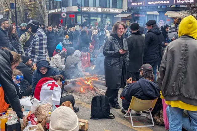 Протестующие в Тбилиси жгут костер на улице, у одного спина накрыта грузинским флагом