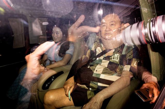 Hình ảnh ông Thaksin ngồi trong ô tô từ bệnh viện trở về nhà, xung quanh bủa vây bởi cánh truyền thông
