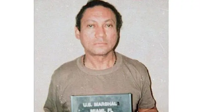 Una fotografía policial del líder militar panameño, Manuel Noriega, con una camisa marrón y mirando directamente a la cámara tras ser arrestado por las autoridades estadounidenses en 1990.