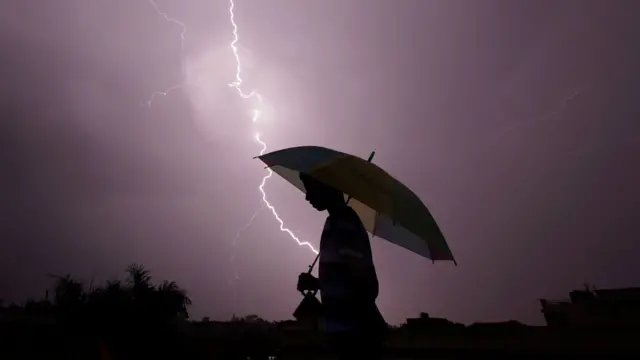 La silueta de un hombre con un paraguas y un rayo en el cielo
