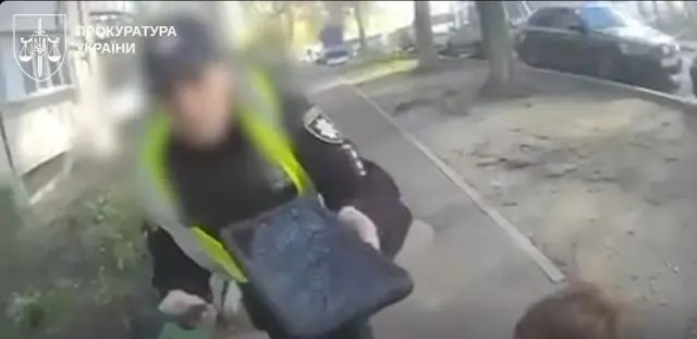 Фото з боді-камери на якому показана жінка-патрульна з планшетом. Обличчя її заблюрене