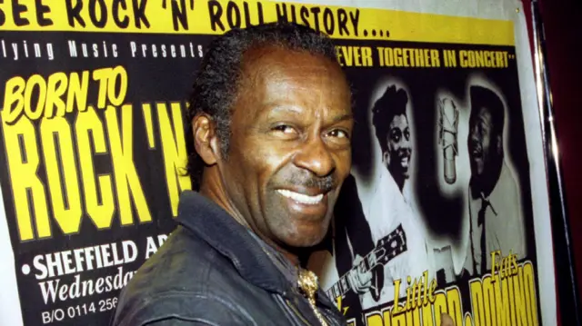 Старий Чак Беррі усміхається на тлі плакату з написом "Born To Rock-n-Roll".