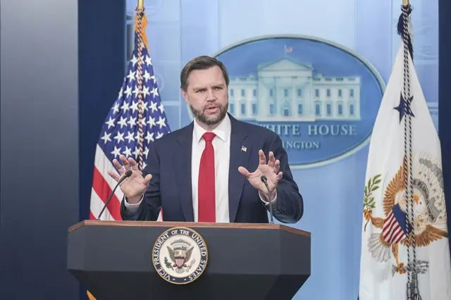 El vicepresidente de EE.UU., JD Vance, habla desde un atril durante una rueda de prensa en la Casa Blanca. Viste traje oscuro, camisa blanca y corbata roja.