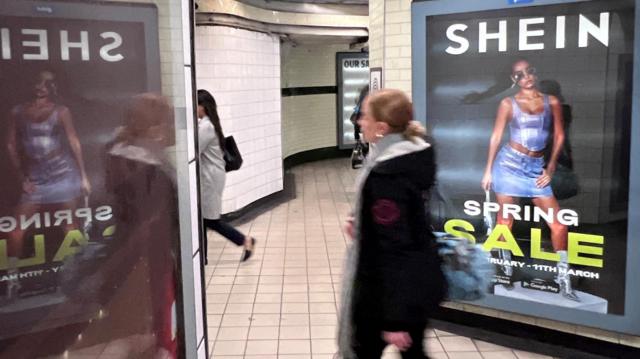 Mulher passa na frente de propaganda da Shein em estação de metrô