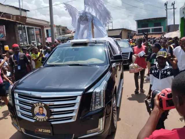 Crowd gather dey watch vehicles wey dey pass during di burial of late Mr Ibu