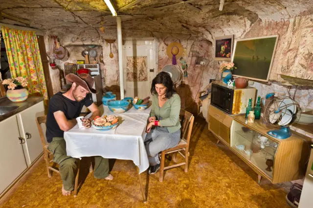 Moradores de Coober Pedy ao redor de mesa em casa subterrânea
