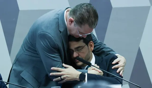 Jorge Messias, sentado, recebe abraço do líder do PL na Câmara dos Deputados, Sóstenes Cavalcante, durante sessão de sabatina no Senado. Na foto, Messias aparece de olhos fechados, em postura contemplativa enquanto é abraçado com os dois braços pelo deputado 