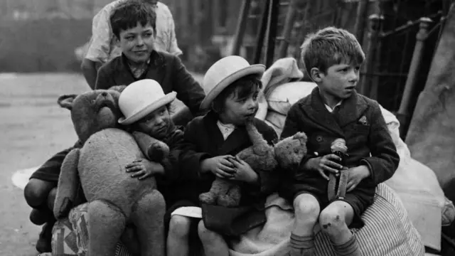 Deca sa igračkama sede skupa, na crno-beloj fotografiji