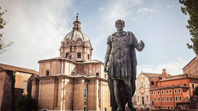 Estátua de Júlio Cesar com construções históricas ao fundo