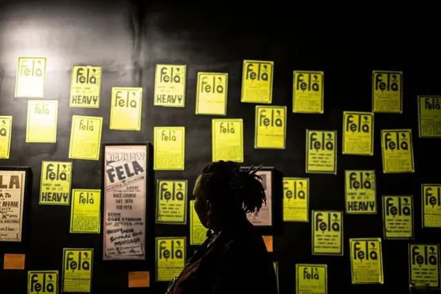 Pesin dey waka pass printouts of di space for newspaper wey Fela dey buy to post im rants for Afrobeat Rebellion exhibition