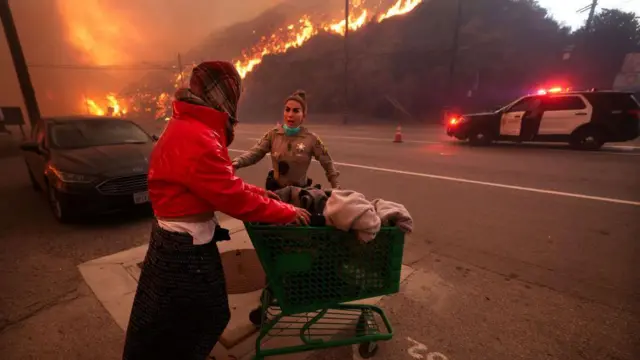 Офіцер поліції супроводжує бездомну жінку для евакуації під час пожежі Палісейдс, штат Каліфорнія, вівторок, 7 січня 2025 року.