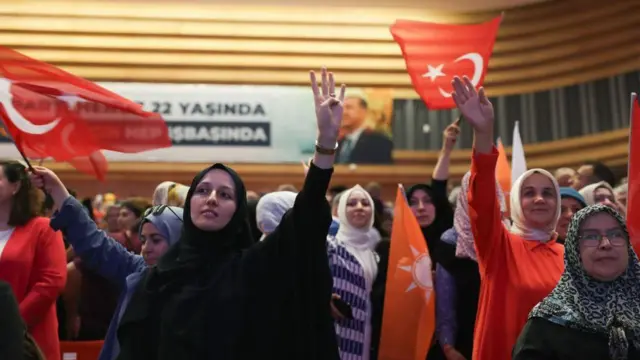 Türk bayrağı ve AKP logolu bayraklar taşıyan kadınlar, arkalarında Erdoğan'ın resmi var