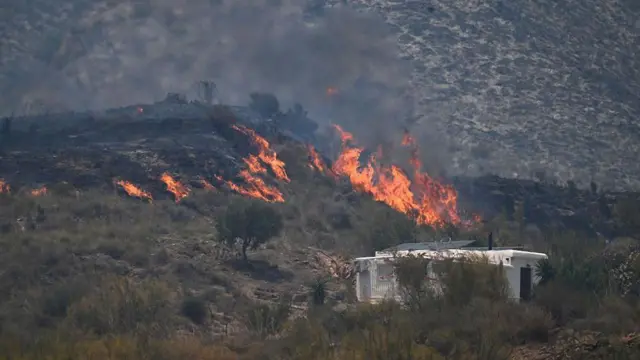 Una imagen tomada el 10 de julio de 2026 muestra llamas en una colina junto a una casa, en la zona de un incendio forestal que causó la muerte de 11 personas cerca de Bédar, en el municipio de Los Gallardos (provincia de Almería).