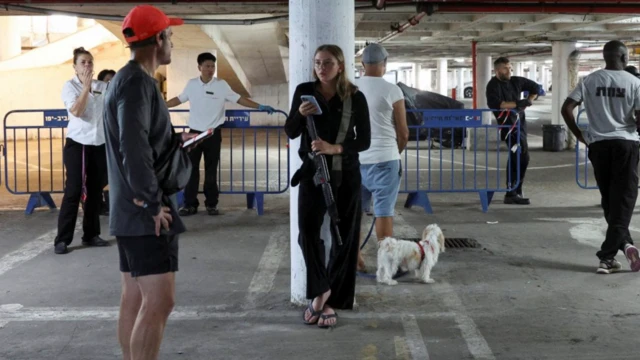 23 Haziran 2025'te İsrail'in Tel Aviv kentinde bir yeraltı otoparkına sığınanlar arasında bir koşucu adam var, bir kadın telefonuna bakıyor. Bir kadın endişeli görünüyor.