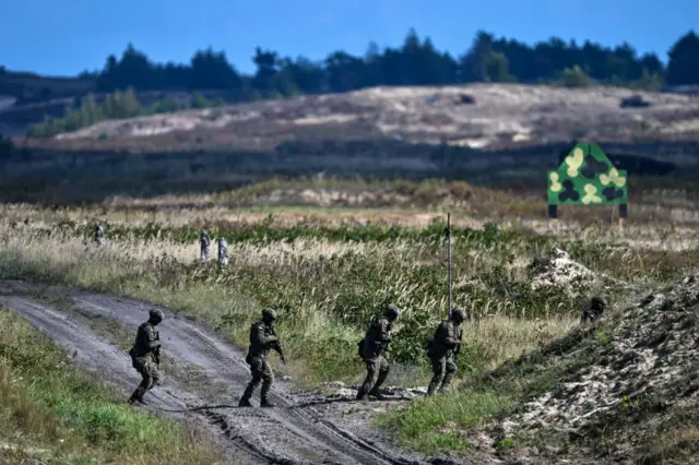 Четверо військових ідуть через ґрунтову дорогу в полі під час навчань