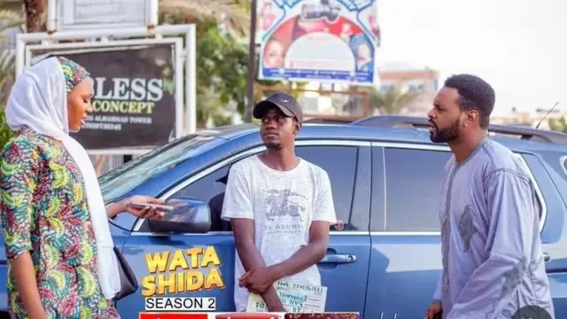 'Yan fim ɗin Wata Shida - mace da maza biyu tsaye a kusa da mota