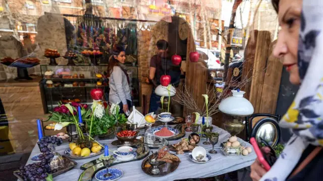 یک سفره «هفت‌سین» — چیدمانی از هفت نماد که نام آن‌ها با حرف «س» آغاز می‌شود — پشت شیشه یک کافه در منطقه مرکزی تجریش تهران، در تاریخ دوشنبه ۲۷ اسفند ۱۴۰۳، در حالی به نمایش گذاشته شده که مردم خود را برای نوروز، سال نو ایرانی، آماده می‌کنند؛ جشنی که امسال با ماه مقدس رمضان همزمان شده است.
این هفت نماد نوروزی عبارت‌اند از: سبزه (جوانه‌هایی که در ظرف رشد داده می‌شوند)، سمنو (پودینگ شیرین از جوانه گندم)، سنجد، سرکه، سیب، سیر و سماق.
میلیون‌ها نفر در خاورمیانه، آسیا و اروپای شرقی جشن نوروز را که معمولاً در اول فروردین برگزار می‌شود، به مناسبت آغاز فصل بهار گرامی می‌دارند.