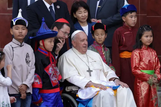El papa Francisco en una silla de rueda rodeado de niños mongoles.
