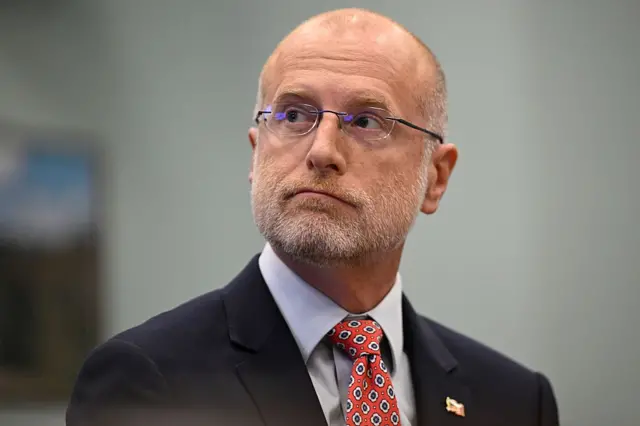 El presidente de la FCC, Brendan Carr, vestido de traje oscuro y corbata roja con diseños, mira de lado. 