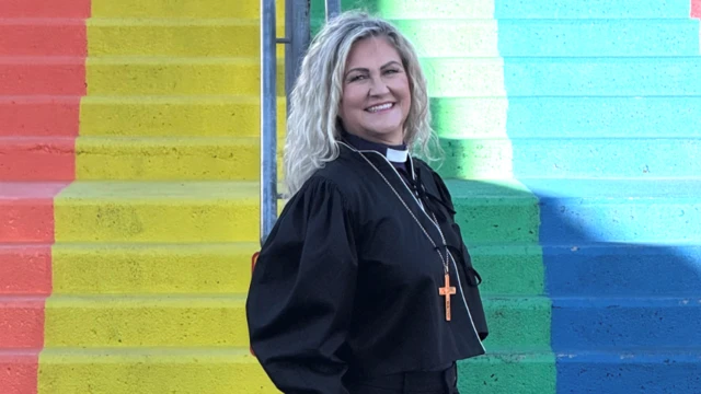 LGBT bayrağı olarak da kullanılan gökkuşağının renklerinde merdivenlerin önünde siyah giyinmiş bir kadın sarı saçları açık şekilde gülerek poz veriyor.