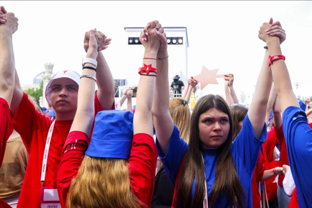 Подростки в синих и красных футболках, браслетах и бейджиках с надписью «Движение Первых» держатся за руки. 