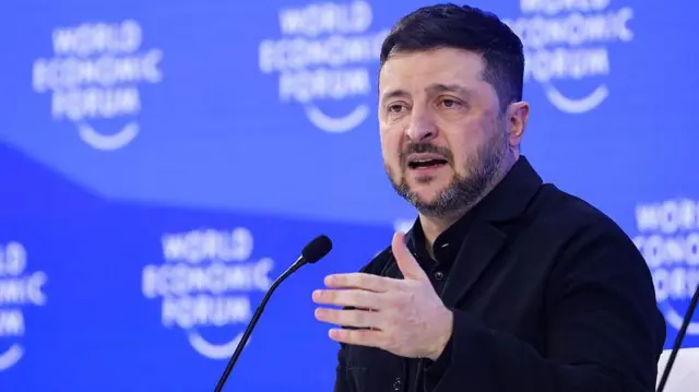 Зеленський жестикулює рукою перед мікрофоном у Давосі, за спиною в нього - логотими форуму на синьому тлі