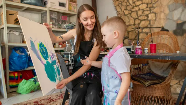 Uśmiechnięta kobieta pokazująca chłopcu obraz w pracowni artystycznej.