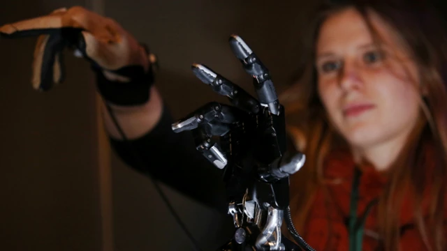 
Uma mulher demonstra uma mão robótica.
