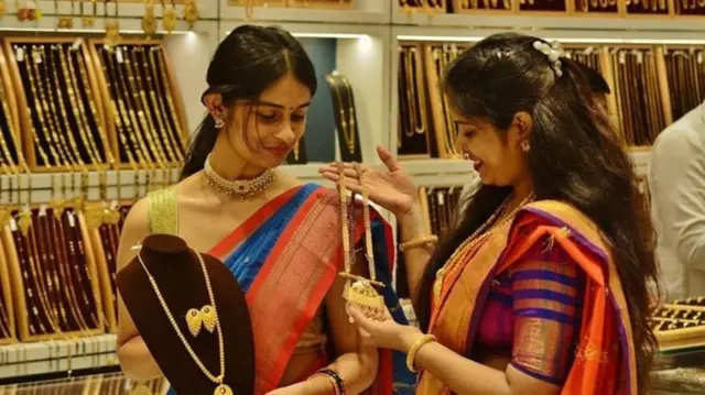 সোনার দোকানে গহনা দেখাচ্ছেন এক নারী অপর নারীকে