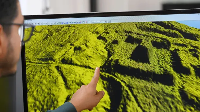 Mano señala un modelo 3D verde de terreno en la pantalla de una computadora.