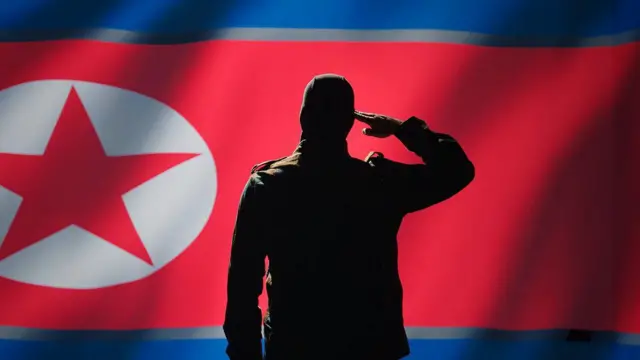 Agen intelijen rahasia memberi hormat dengan gestur tangan ke arah bendera Korea Utara di ruang perang, menunjukkan rasa hormat.