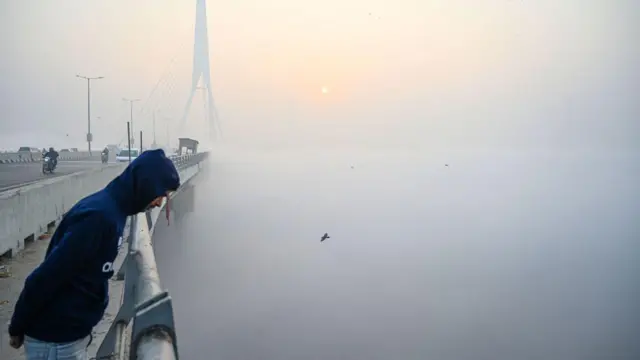 सर्द हवाओं और स्मॉग के बीच दिल्ली में पुल से नीचे झांकता एक आदमी 