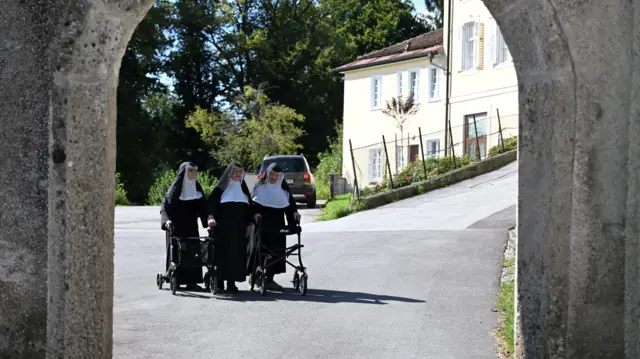 سه خواهر راهبه در حال قدم زدن با واکرهای خود جلوی ساختمان صومعه هستند