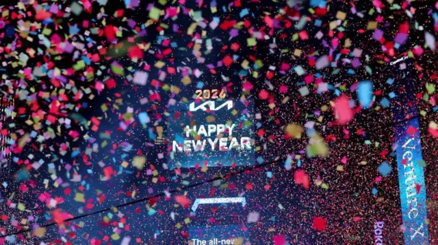 「2026 Happy New Year」と書かれた電光掲示板の周りに、色とりどりの紙吹雪が飛び交っている