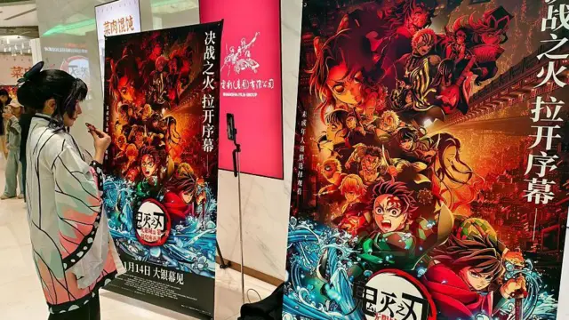 「劇場版『鬼滅の刃（やいば）』無限城編 第一章 猗窩座（あかざ）再来」の中国プレミアで、コスプレをしたファンが菓子を食べながらポスターを眺めている。
