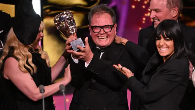 Alan Carr, Paloma Faith ve Claudia Winkleman sahnede ödülü kaldırıp gülümsüyor