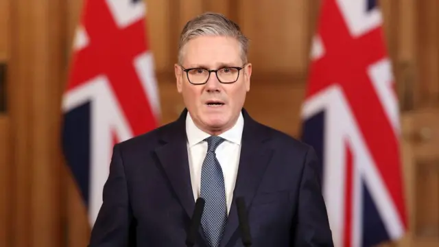 İngiltere Başbakanı Starmer, İran'a yönelik ortak ABD-İsrail saldırılarının ardından makamında açıklama yapıyor, arka planda Birleşik Krallık bayrakları görünüyor, Londra, 28 Şubat 2026